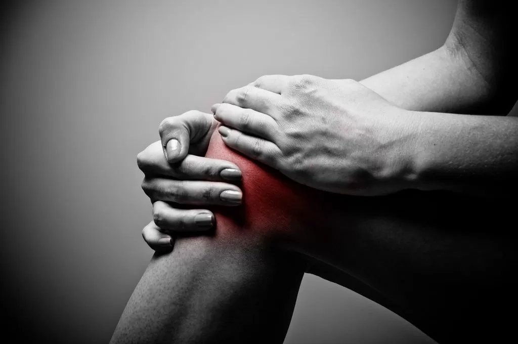 Person holding their knee in pain. Black and white image. Click Physiotherapy