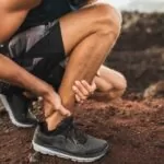 Achilles injury on running outdoors. Man holding Achilles tendon by hands close-up and suffering with pain. Sprain ligament or Achilles tendonitis.